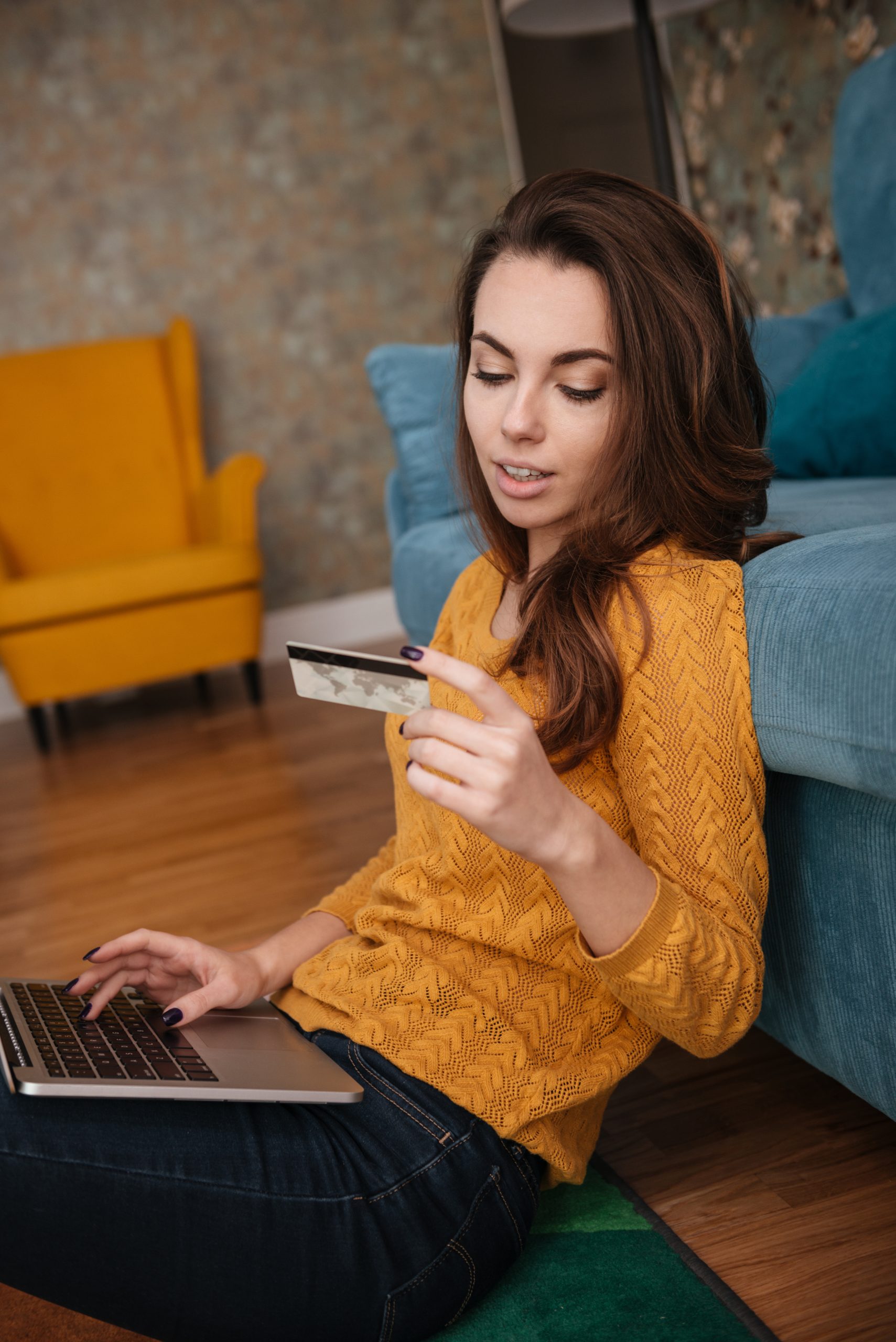 graphicstock portrait of a woman shopping on line holding credit card and typing on a laptop while sitting in the living room at home HO uqiKFpx scaled