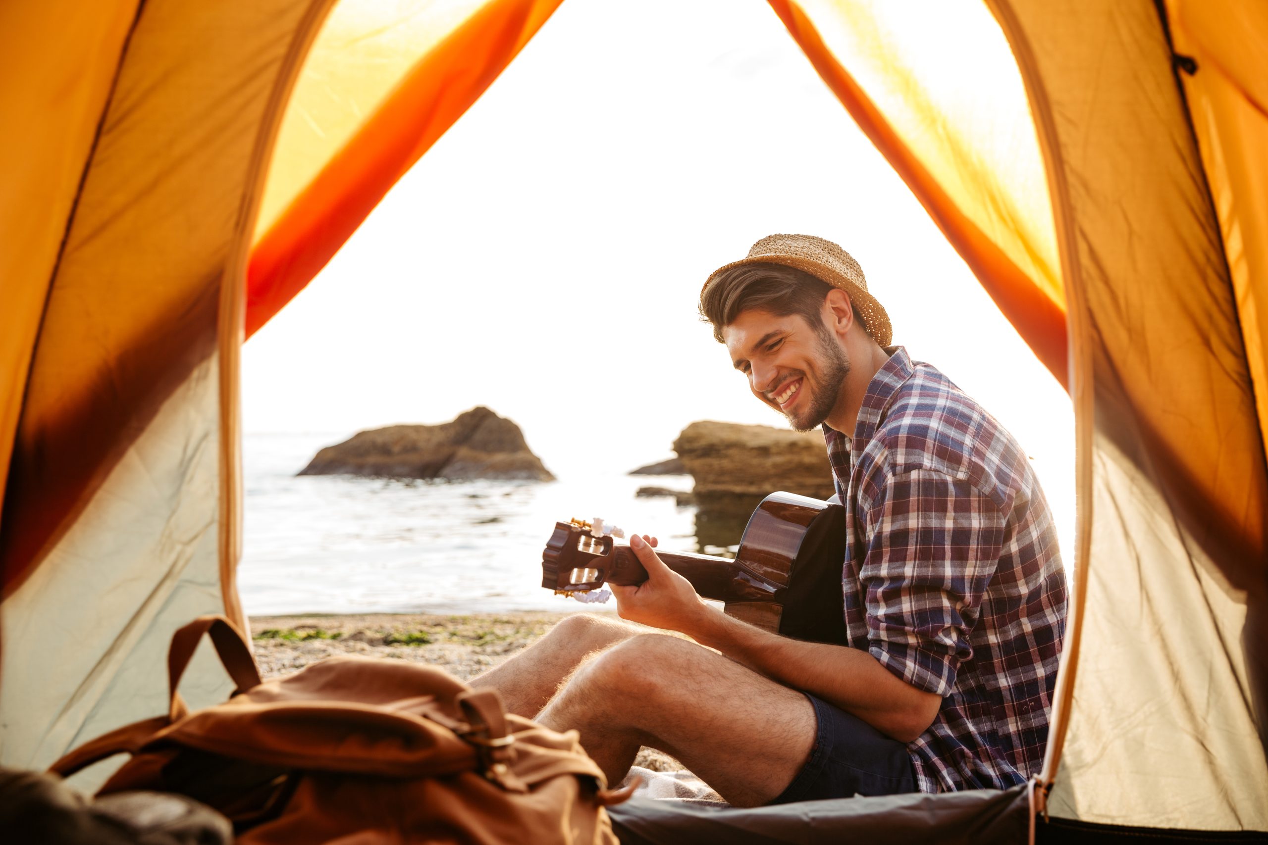 graphicstock smiling young man sitting near touristic tent and playing guitar at the beach HuBaB7HH3x scaled