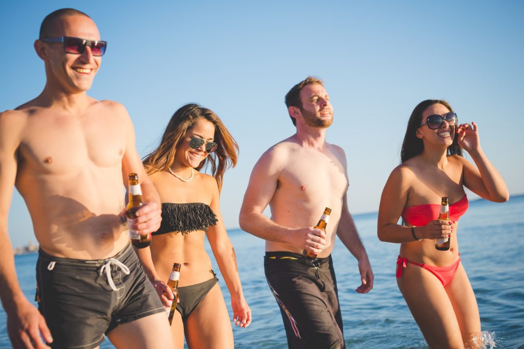 graphicstock group of young multiethnic friends women and men at the beach in summertime waliking on the foreshore smiling from front with beers in their hands team friendship tourism concept HThrI5FJZ