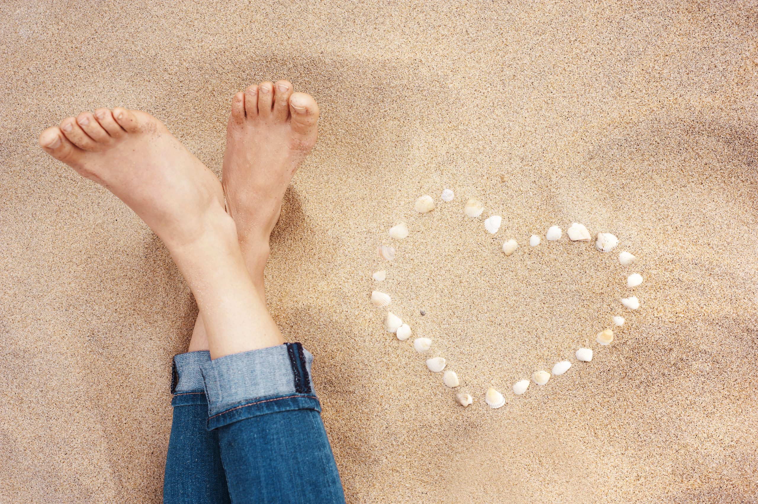 graphicstock female feet closeup of woman standing at the sandy beach next to the shell heart S0OghonZZ scaled